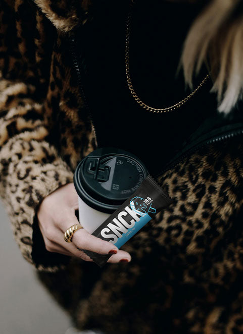 Person holding a coffee cup with a SNCK bar, wearing a leopard print sleeve.