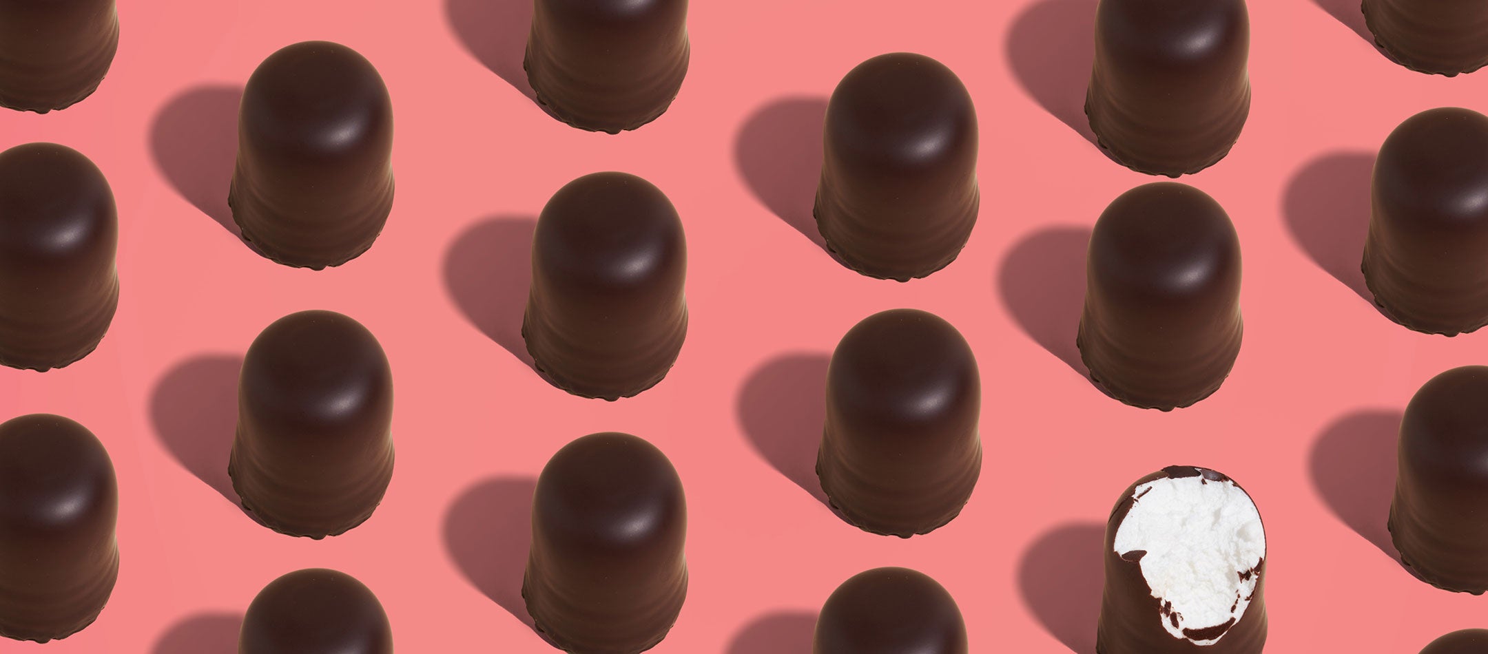 Chocolate candies with one having a white filling on a pink background