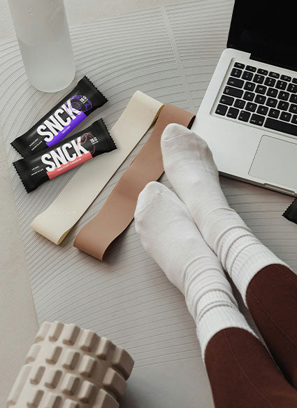 Person wearing socks with SNCK protein bars and a laptop on a desk
