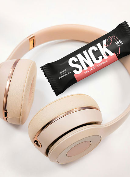 Beige headphones with a SNCK protein bar on a white background